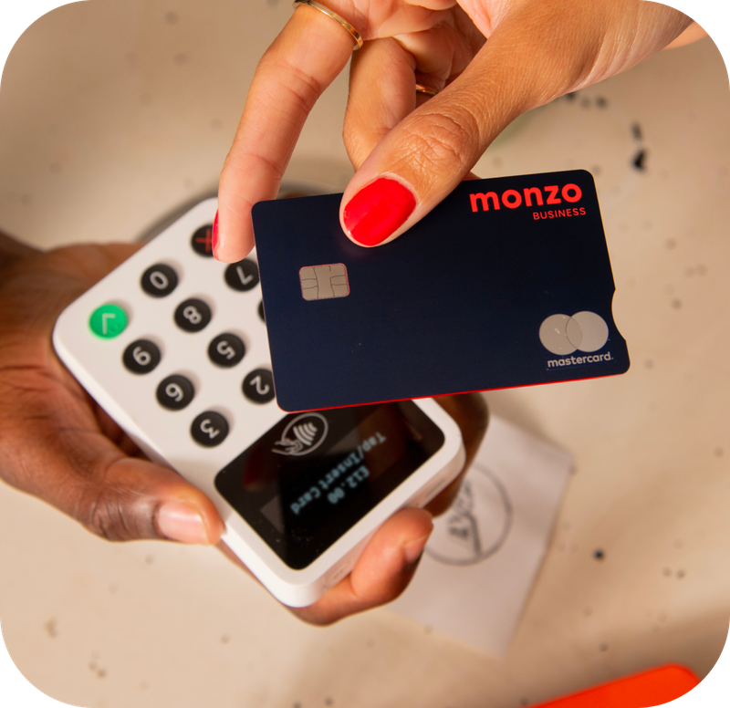 A hand with red nail polish is holding a Monzo Business card over a payment terminal.