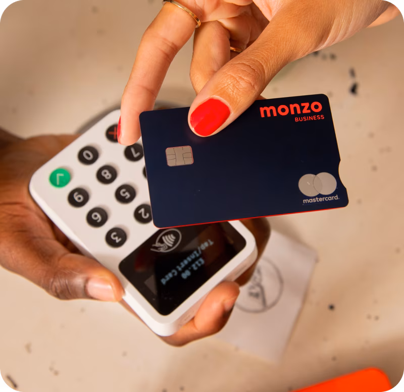 Un cliente paga con la tarjeta azul marino de Monzo Business acercándola al lector de tarjetas que sujeta otra persona.