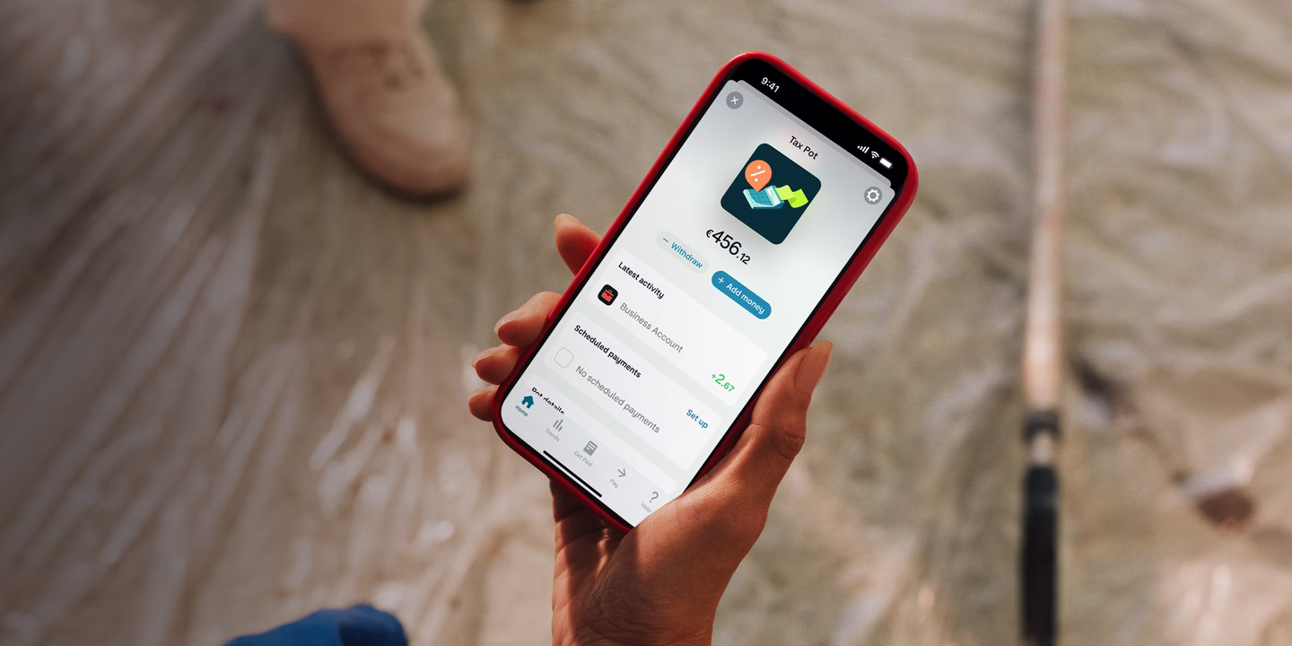 Person on a construction site holding a phone in a red case, showing their Monzo Business Tax Pot with a €456.12 balance and recent activity.