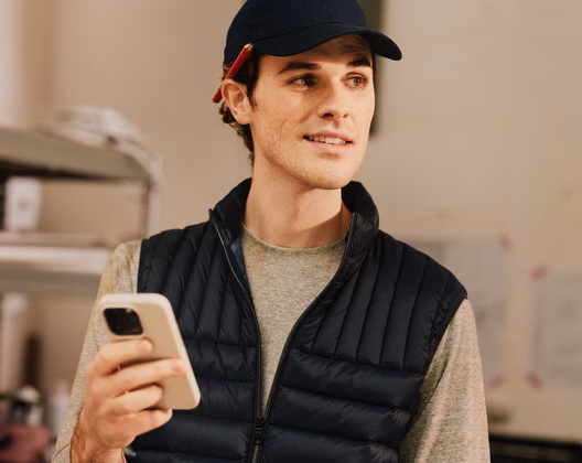 Tradesperson in work gear holding their phone and smiling, ready to manage their business on the go from a construction site.