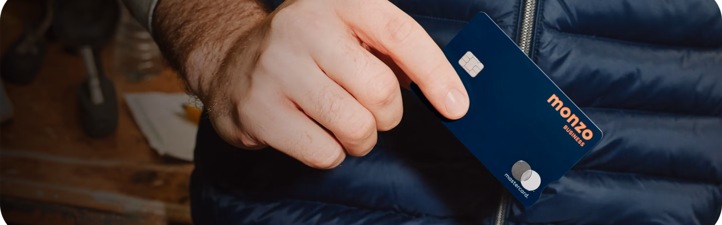 A hand holding a navy Monzo Business card.