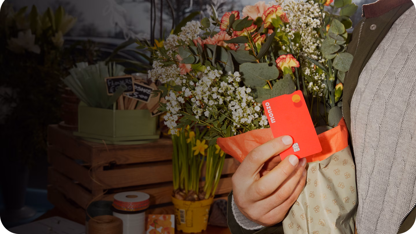 Someone holding their Hot Coral Monzo card against some bright blooms.
