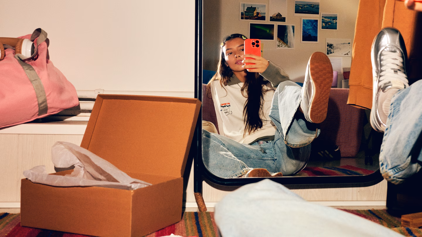 A teenager relaxes with her feet up, taking a mirror selfie on her phone in her bedroom
