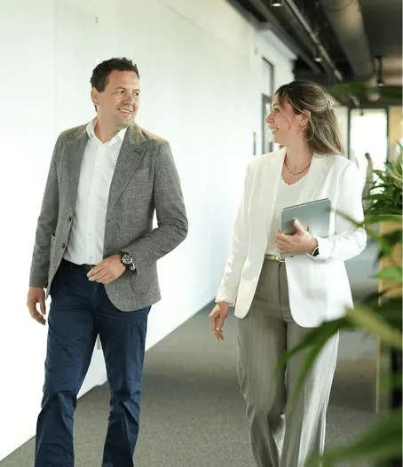 Zwei Mitarbeitende stimmen sich während eines gemeinsamen Rundgangs durch das Büro zu einem Projekt ab und koordinieren die nächsten Schritte der Projektsteuerung.
