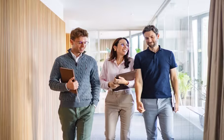 Drei Studierende laufen durch ein modernes Büro zu einem Termin