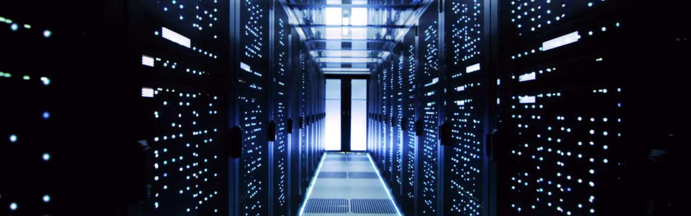 Ein beleuchteter Serverraum mit Reihen von schwarzen Schränken voller blinkender Lichter. Die Perspektive verläuft in die Tiefe des Raumes.