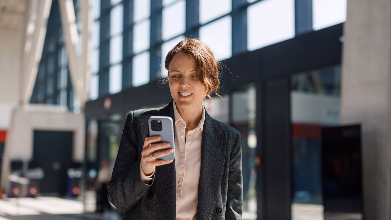 Geschäftsfrau checkt ihr Smartphone, während sie während des Arbeitswegs durch eine moderne Lobby geht