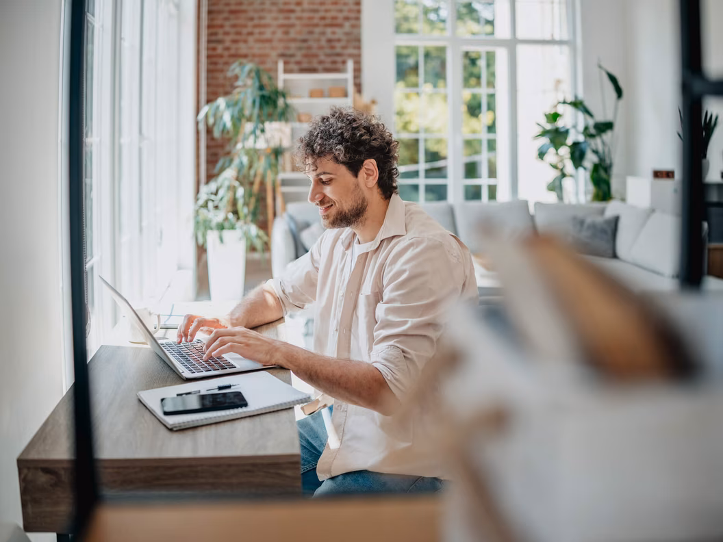 Young man working from home in a modern living room, focused on his laptop and getting tasks done