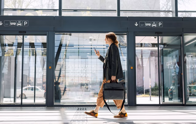 Frau läuft mit Handy und Aktentasche durch einen modernen Bahnhof