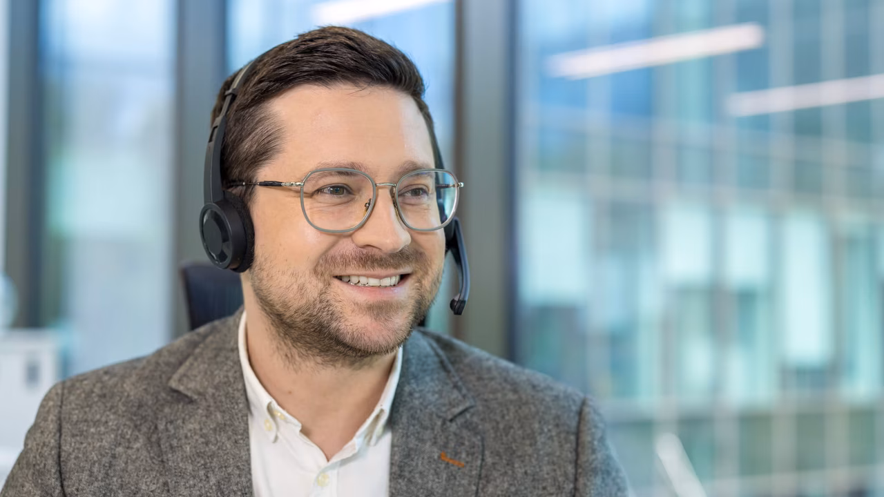 Eine Nahaufnahme eines lächelnden Mannes mit Headset und Brille, der lächelnd in einem Büro arbeitet im Kontext professioneller Managed Services