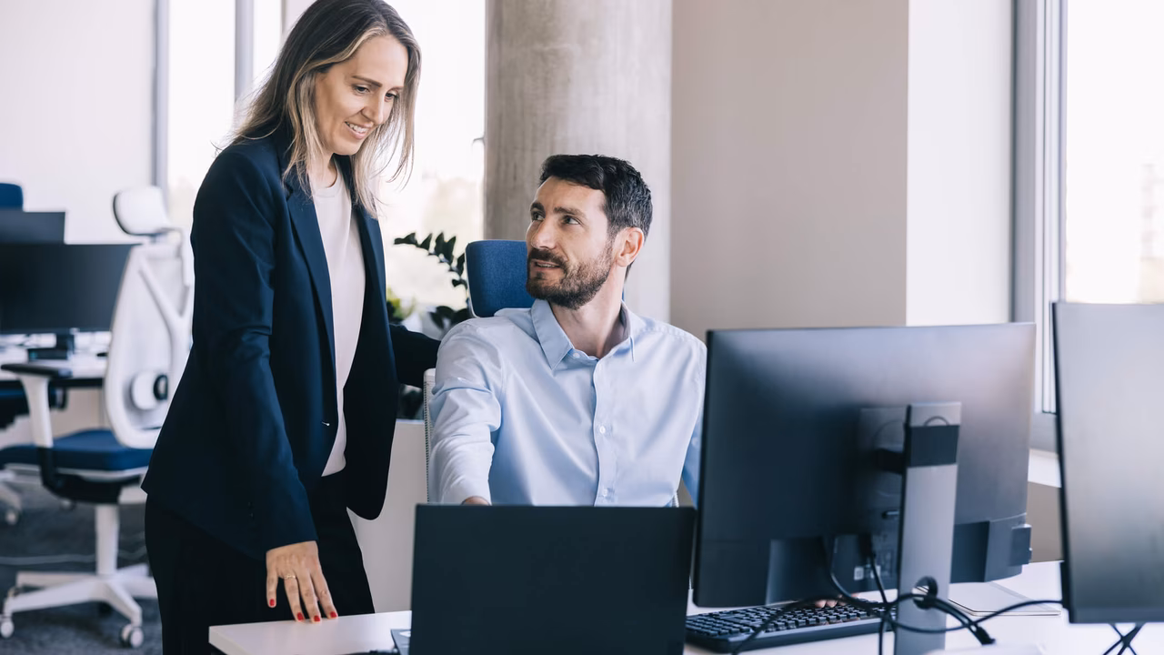 Two employees working together on a laptop and screen with collaboration software