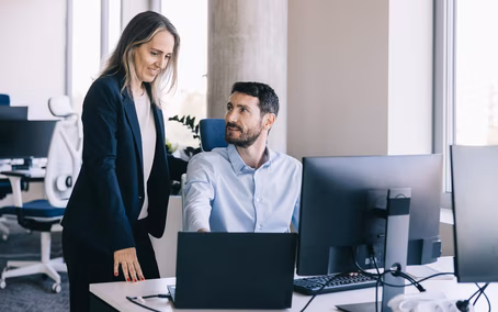 Two employees working together on a laptop and screen with collaboration software