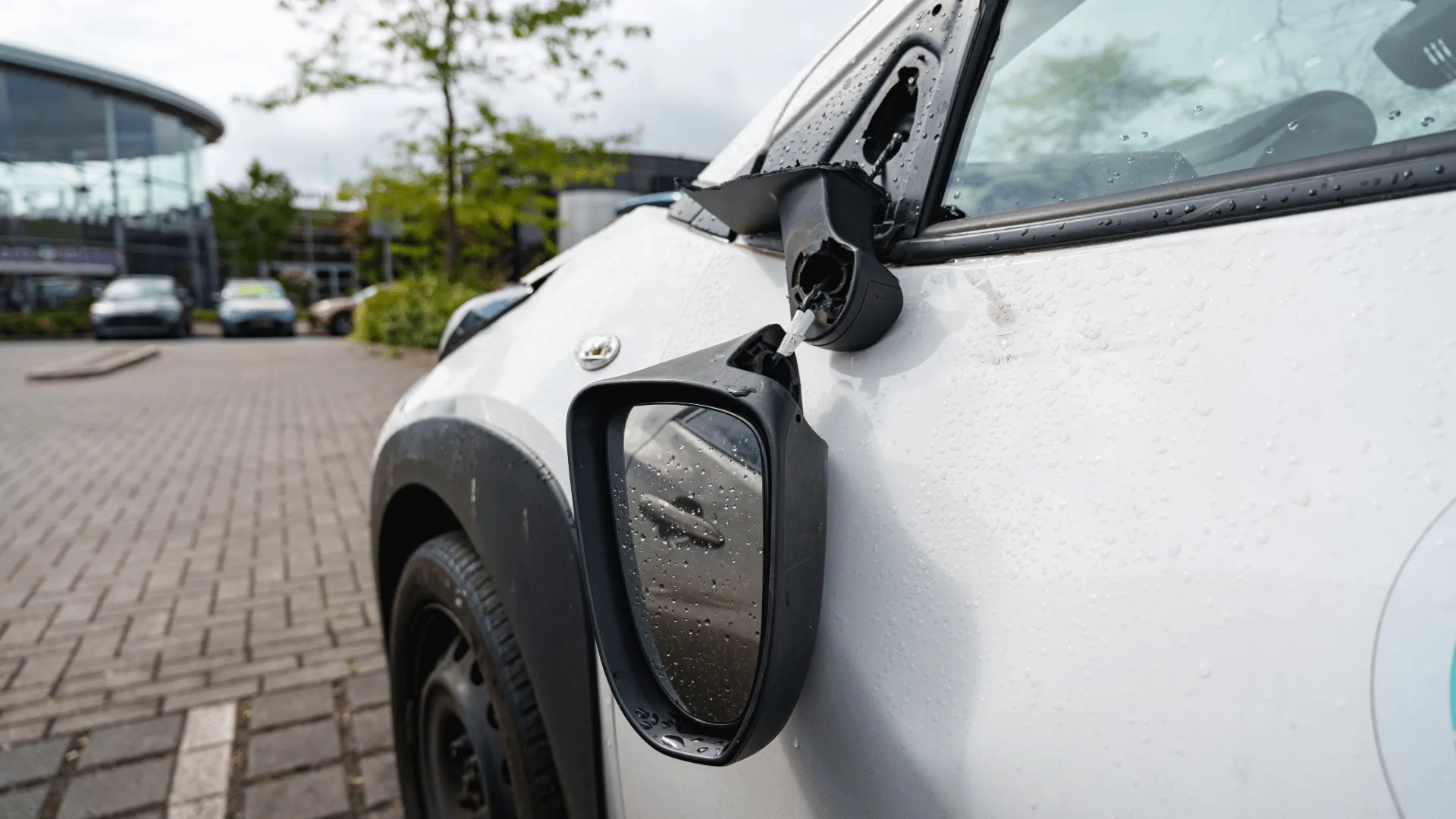 A close-up of a broken wing mirror hanging off a white car, illustrating the type of accidental damage where excess protection covers your insurance claim costs.