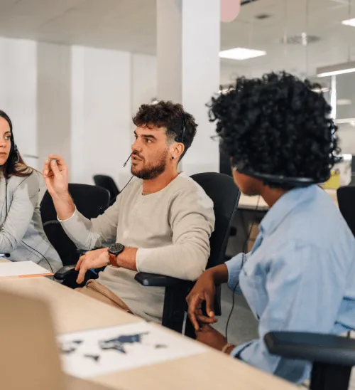 A diverse team of insurance advisors wearing headsets engaged in a collaborative discussion at a desk in a bright, modern office.