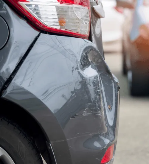 A close-up of a deeply dented and scratched rear bumper on a grey car, representing a common vehicle damage claim.