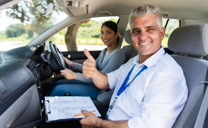 Happy driving instructor in the car with his pupil after saving money on his insurance
