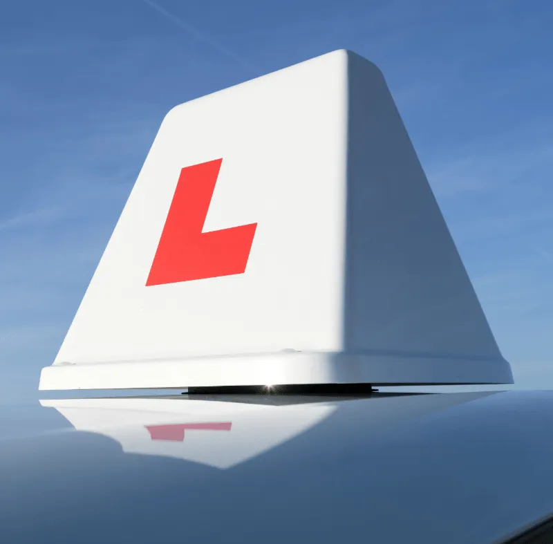 Close-up of a white learner driver roof sign with a red L against a clear blue sky.