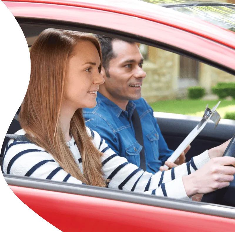 A learner driver and a driving instructor sitting inside a red dual-control tuition vehicle during a driving lesson.