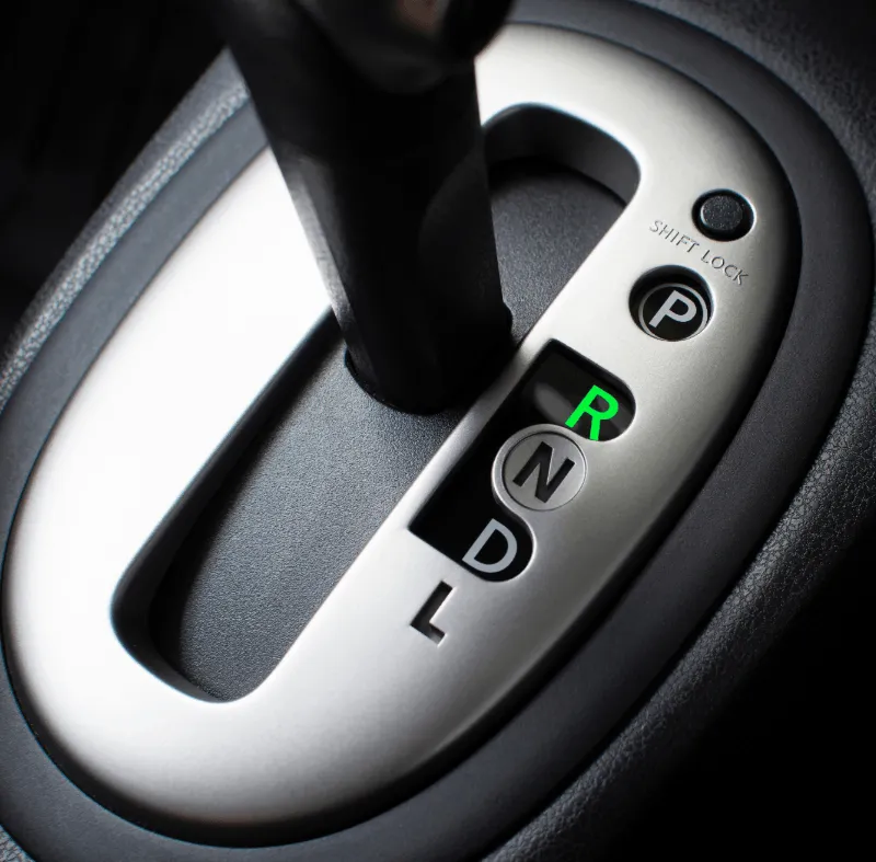 Close-up of a car’s automatic gear shift in reverse, with the “R” indicator lit green.
