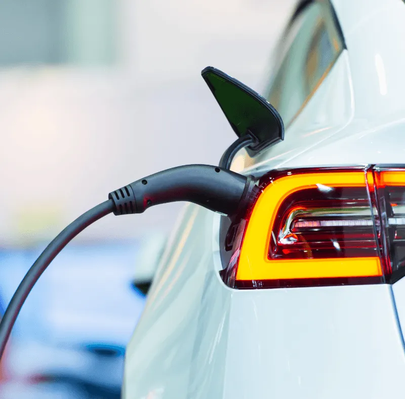 Close-up of an electric car being charged, with a power cable plugged into the rear taillight area.