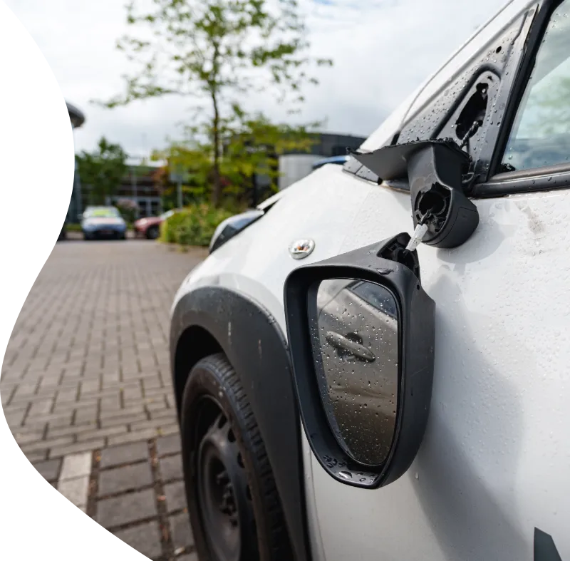 A close-up of a broken wing mirror hanging off a white car, illustrating the type of accidental damage where excess protection covers your insurance claim costs.
