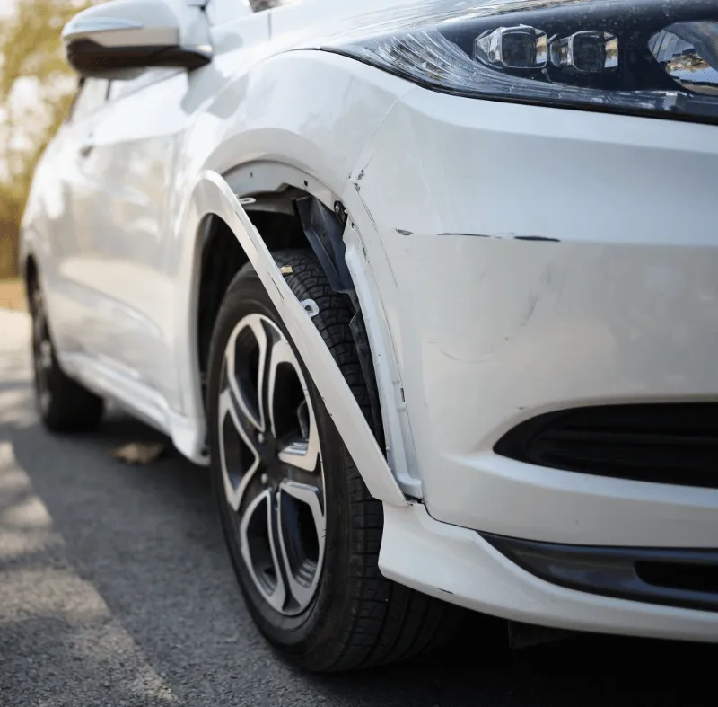 Damaged white car with scratches and a broken wheel arch, representing learner driver accidents and driving instructor insurance claims.