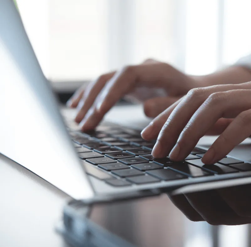 Close-up of a person’s hands typing on a laptop keyboard in a bright, modern workspace.