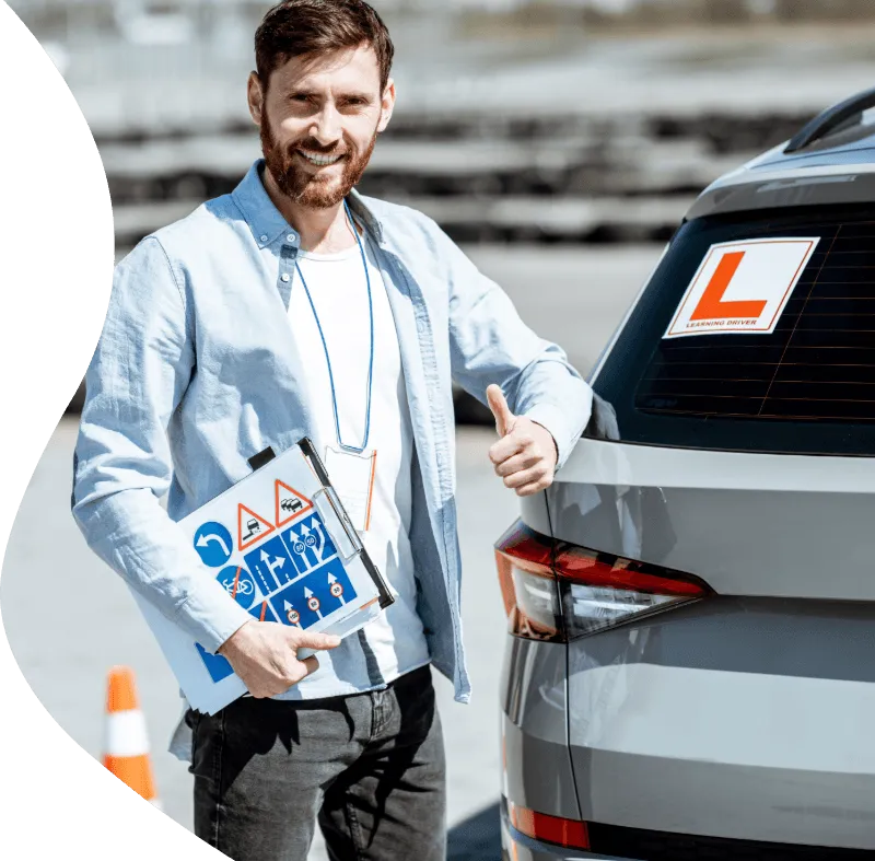 Smiling driving instructor holding road sign folder gives thumbs-up beside car displaying a learner “L” plate.