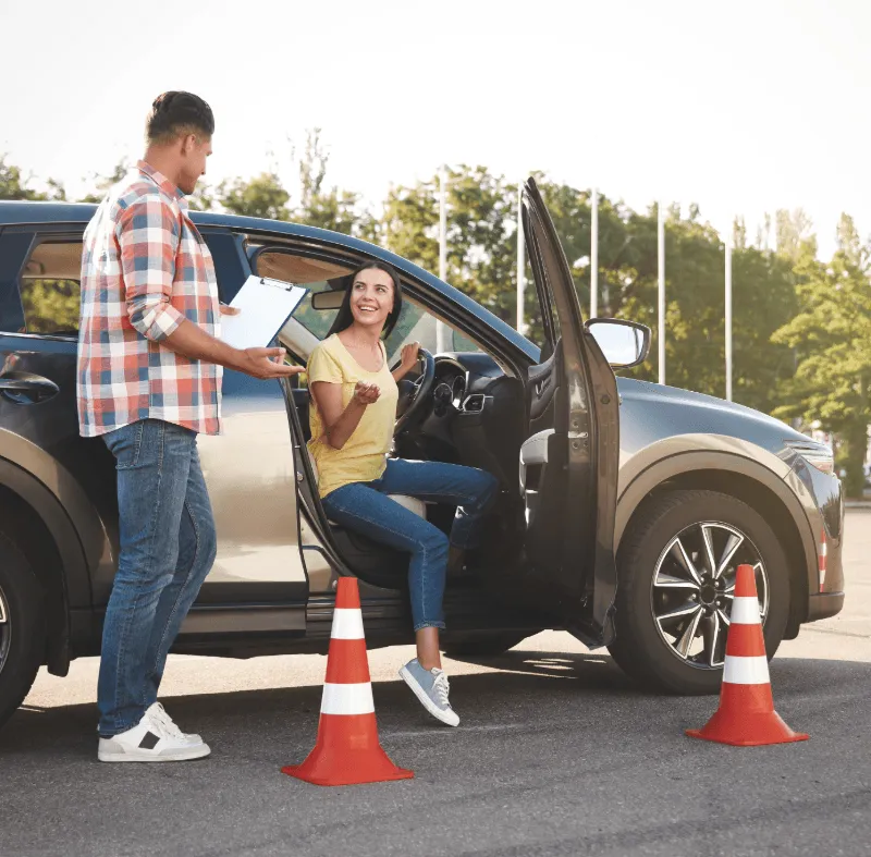 Driving instructor speaking with a learner driver beside a car with training cones, representing driving school insurance and learner driver cover.