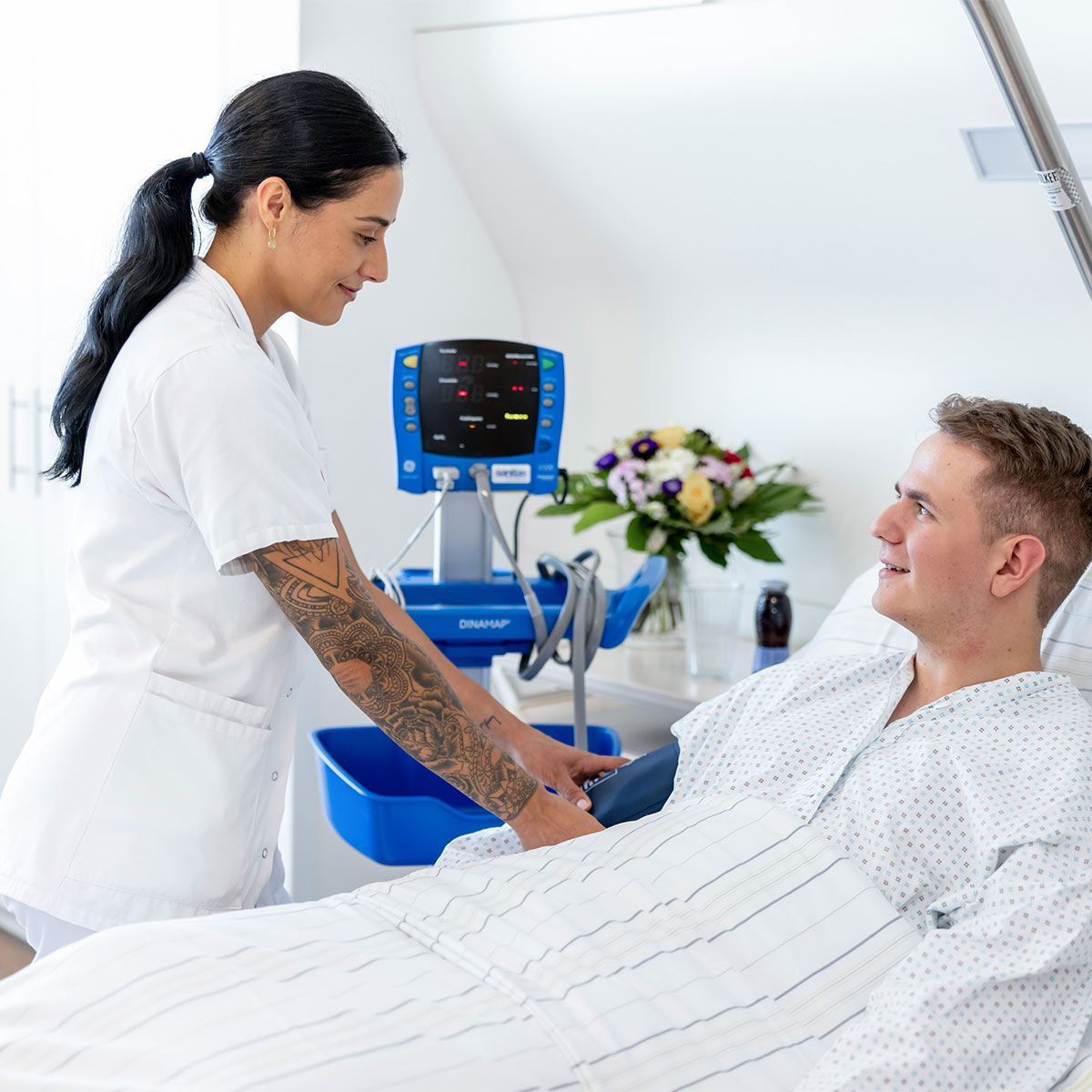 Pflegeperson steht bei Patient am Bett