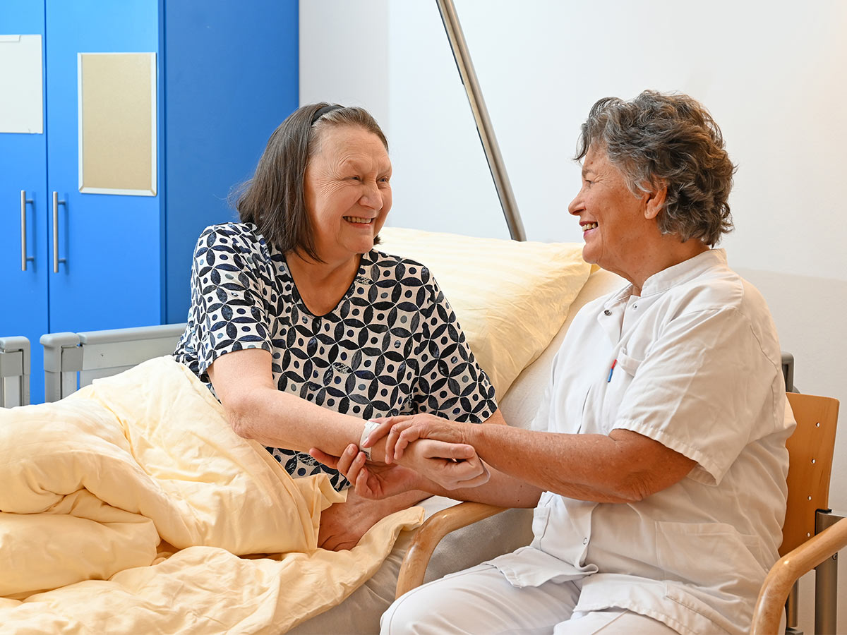 Ehrenamtliche Mitarbeiterin sitzt bei Patientin am Bett