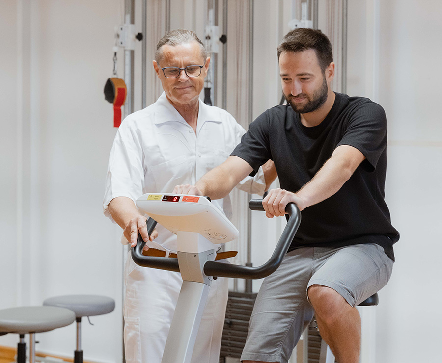 Patient trainiert am Rad, daneben ein Mediziner