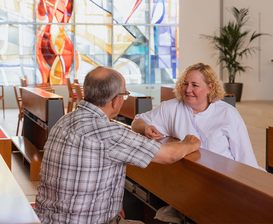 Seelsorgerin im Gespräch mit einem Patienten in der Kapelle