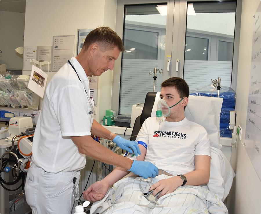 Pfleger betreut jungen Patienten mit Sauerstoffmaske in der Notaufnahme, medizinische Geräte im Hintergrund