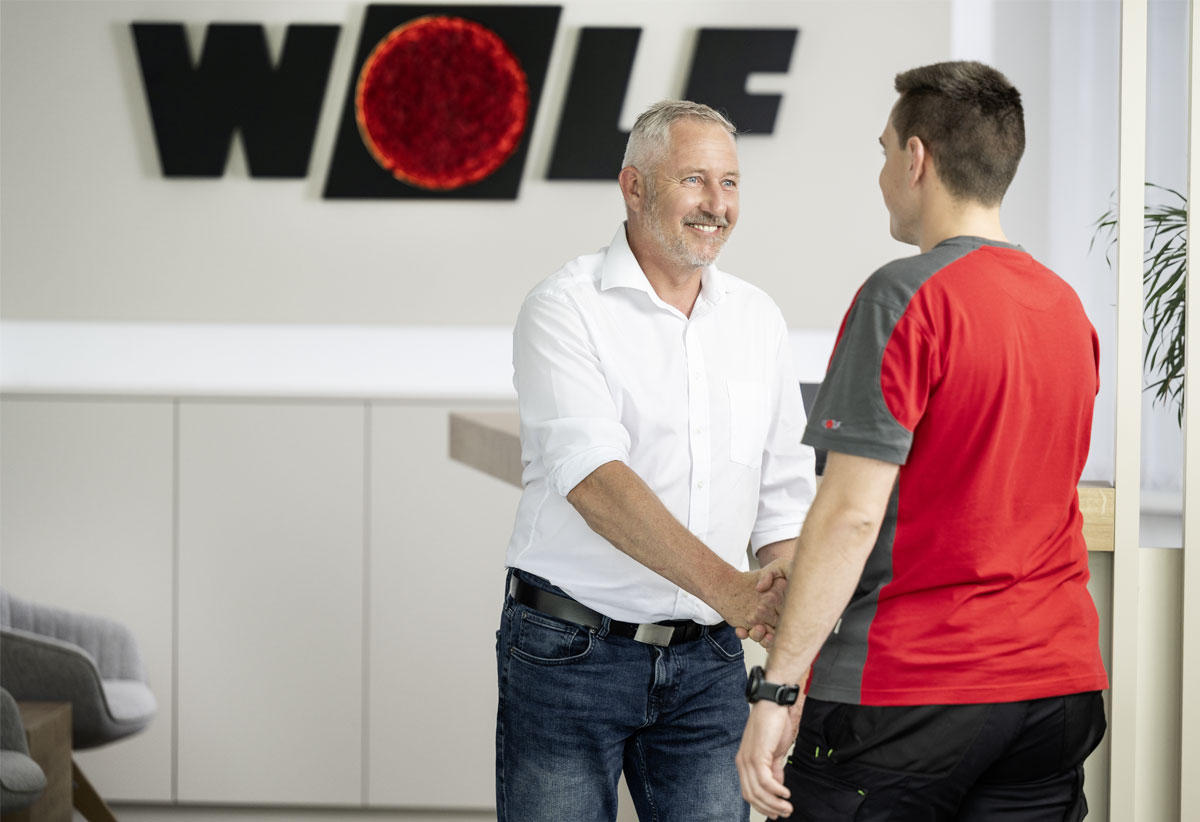 Servicetechniker gibt Kunde die Hand; dahinter Firmenfahrzeug mit WOLF Werkskundendienst Branding