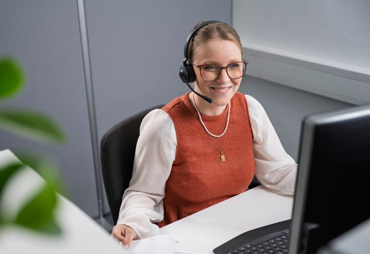 Freundliche junge Frau mit Headset vor Bildschirm