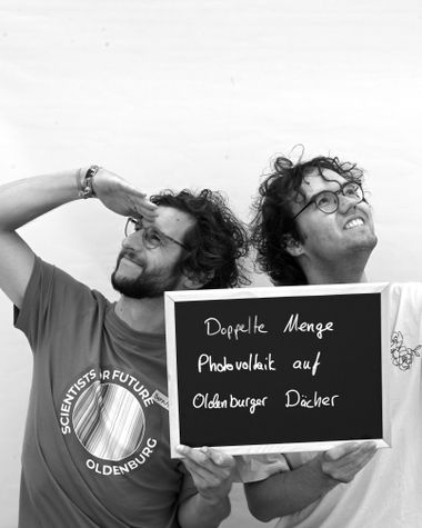 Zwei Personen aus Oldenburg zeigen ein Schild auf dem steht „Doppelte Menge Photovoltaik auf Oldenburger Dächer“ Foto: Jörg Hemmen