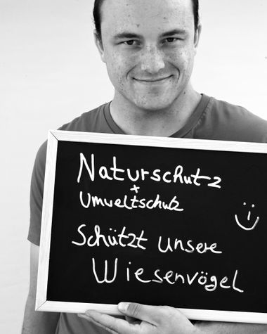 Eine Person aus Oldenburg zeigt ein Schild auf dem steht „Naturschutz + Umweltschutz schützt unsere Wiesenvögel“ Foto: Jörg Hemmen