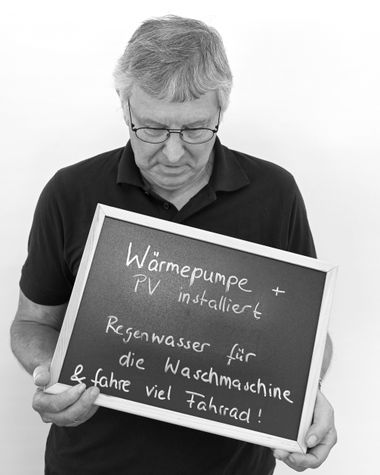 Eine Person aus Oldenburg zeigt ein Schild auf dem steht: „Wärmepumpe und Photovoltaik installiert. Regenwasser für die Waschmaschine und fahre viel Fahrrad!“ Foto: Jörg Hemmen