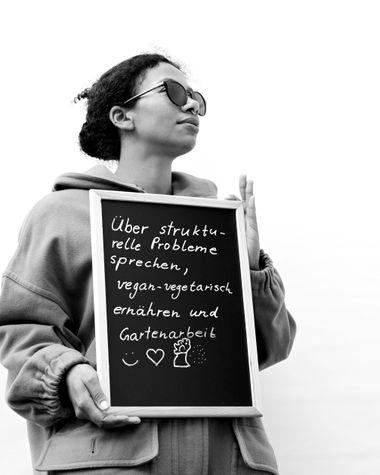 Eine Person aus Oldenburg zeigt ein Schild auf dem steht „Über strukturelle Probleme sprechen, vegan-vegetarisch ernähren und Gartenarbeit“ Foto: Jörg Hemmen