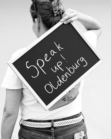 Eine Person aus Oldenburg zeigt ein Schild auf dem steht „Speak up Oldenburg!“ Foto: Jörg Hemmen