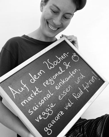 Eine Person aus Oldenburg zeigt ein Schild auf dem steht: „Auf dem Wochenmarkt regional & saisonal einkaufen, veggie essen und ganz viel Rad fahren!“ Foto: Jörg Hemmen