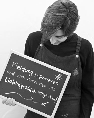 Eine Person aus Oldenburg zeigt ein Schild auf dem steht „Kleidung reparieren und sich dabei neu ins Lieblingsstück vergucken!“ Foto: Jörg Hemmen