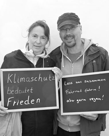 Zwei Personen aus Oldenburg zeigen jeweils ein Schild auf denen steht „Klimaschutz bedeutet Frieden“ und „Lass uns zusammen Fahrrad Fahren! Aber gern vegan!“ Foto: Jörg Hemmen