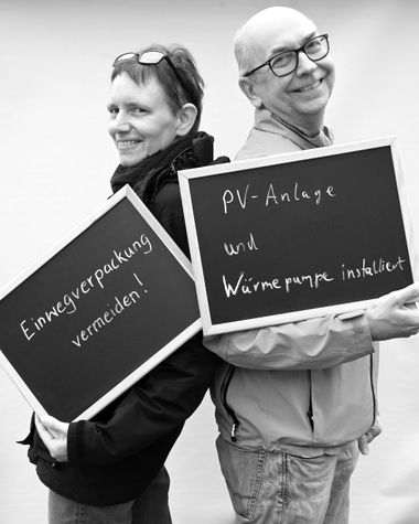 Zwei Personen aus Oldenburg zeigen jeweils ein Schild auf denen steht „Einwegverpackungen vermeiden!“ und „PV-Anlage und Wärmepumpe installiert“ Foto: Jörg Hemmen