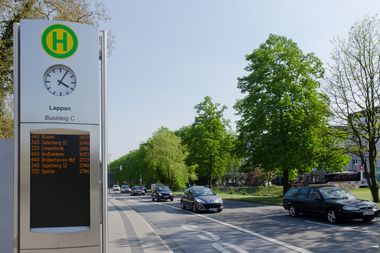 Blick auf eine Straße an der die digitale Anzeige einer Bushaltestelle die nächsten Busse anzeigt.