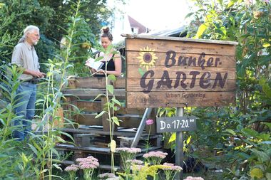 Eingangsschild des Bunkergartens, dahinter ein Einblick in den Garten.