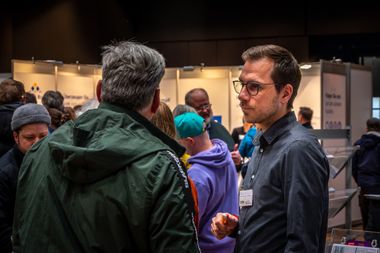 Zu sehen ist eine Beratungssituation auf einer Messe. Zwei Menschen unterhalten sich im Vordergrund, im Hintergrund sind viele weitere zu sehen. Foto: Stadt Oldenburg