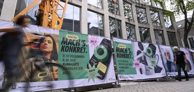 Banner an einem Bauzaun vor einem Haus mit „Mach's. Konkret“-Kampagne