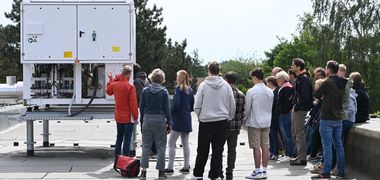 Zu sehen ist eine Gruppe Menschen, die vor einer Großwärmepumpe auf einem Dach stehen und Informationen dazu erhalten. Foto: Jörg Hemmen